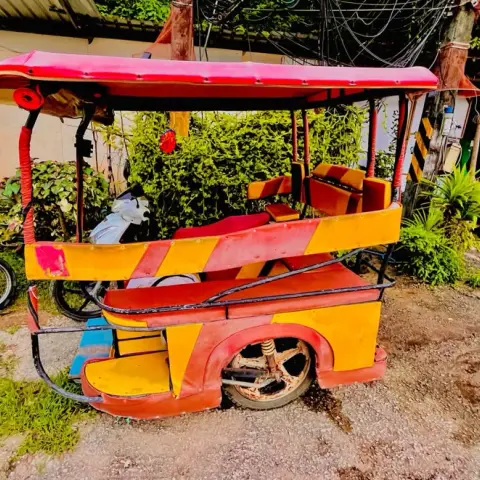 A red and yellow tuk-tuk with bench seats parked on grass