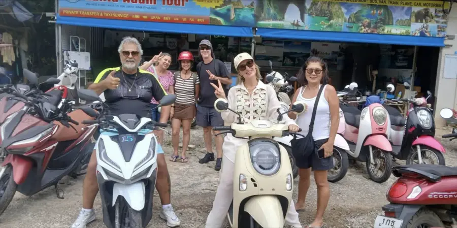 A group of smiling visitors with rental scooters outside the Lanta Adam Tour shop