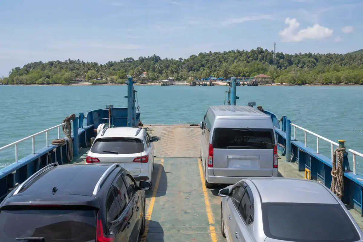 Vehicles on a ferry crossing towards a low forested island coastline