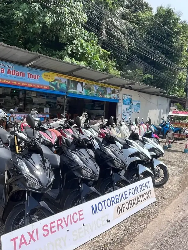 Scooters lined up in front of the shop with a banner reading Taxi service, Motorbike for rent, Information